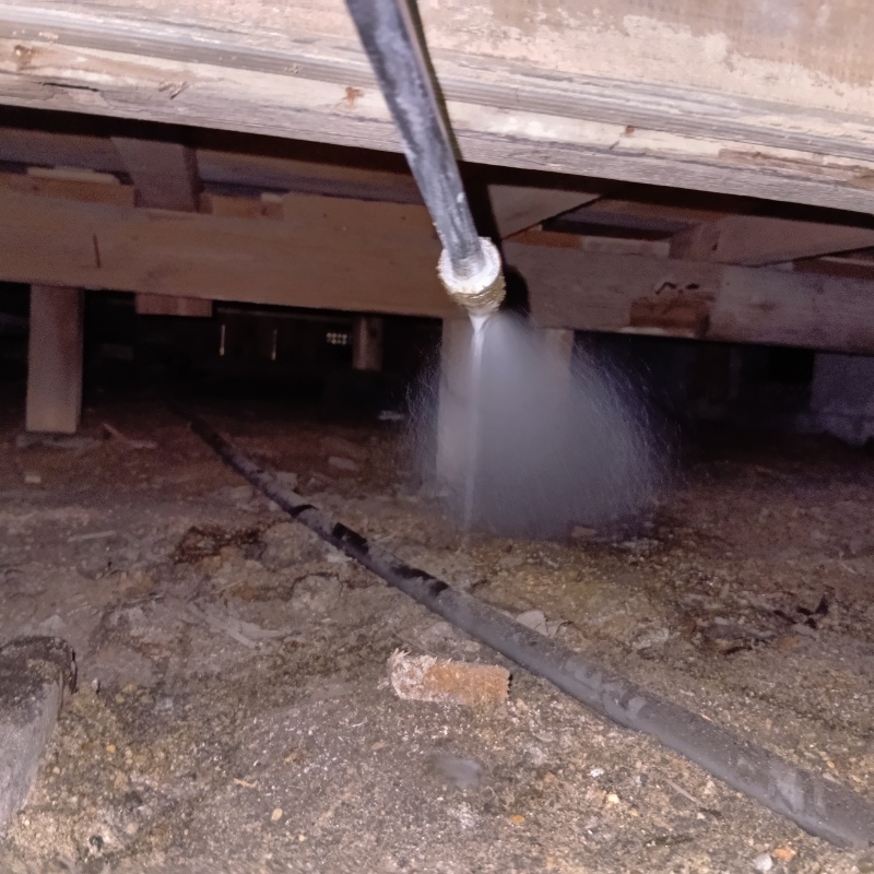 床下の地面にシロアリ駆除剤を吹きつけている様子