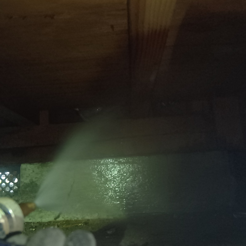 床下の地面にシロアリ駆除剤を吹きつけている様子