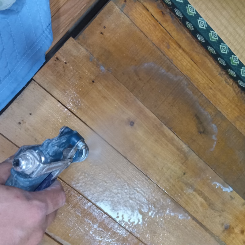木製のフローリングにシロアリ駆除剤を吹き付ける様子