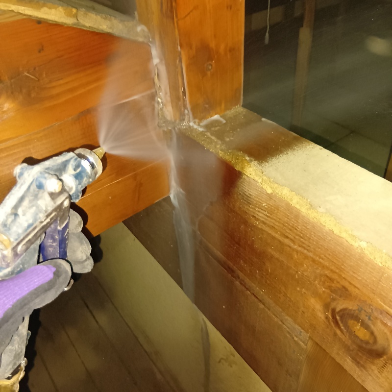 屋根裏の木材にシロアリ駆除剤を吹き付ける様子