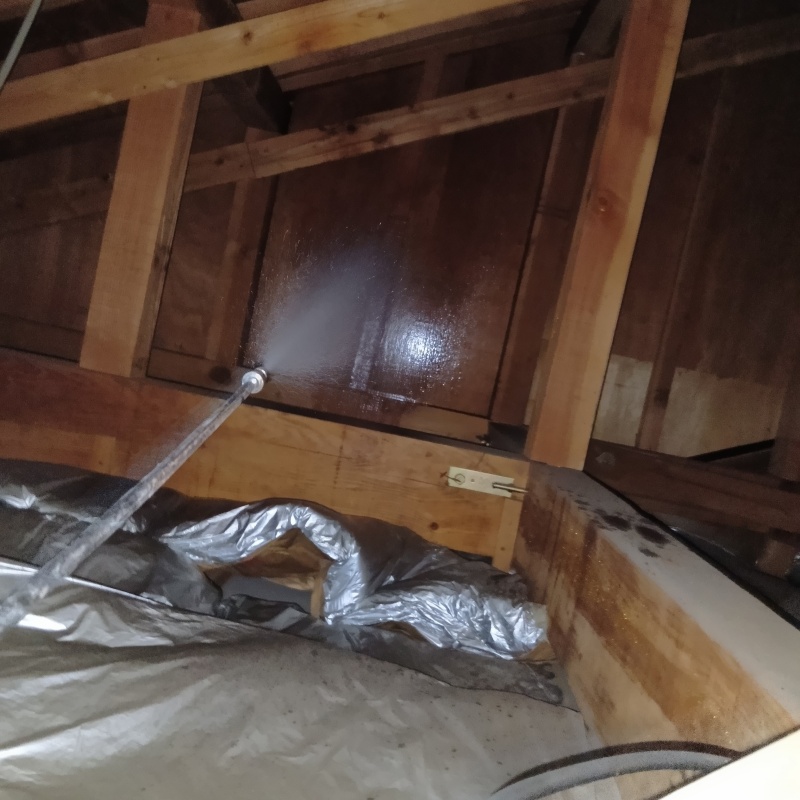 屋根裏の木材にシロアリ駆除剤を吹きつけている様子