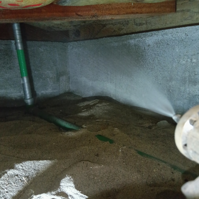 床下の基礎部分にシロアリ駆除剤を吹きつけている様子