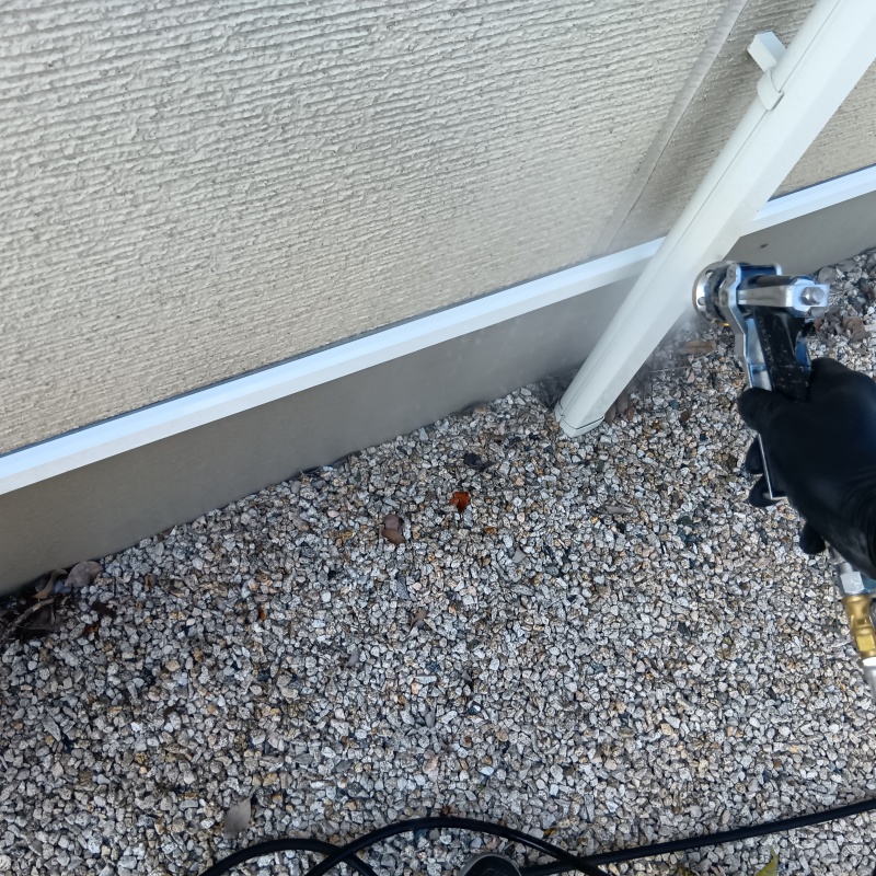 外壁や砂利にシロアリ駆除剤を吹きつけている様子