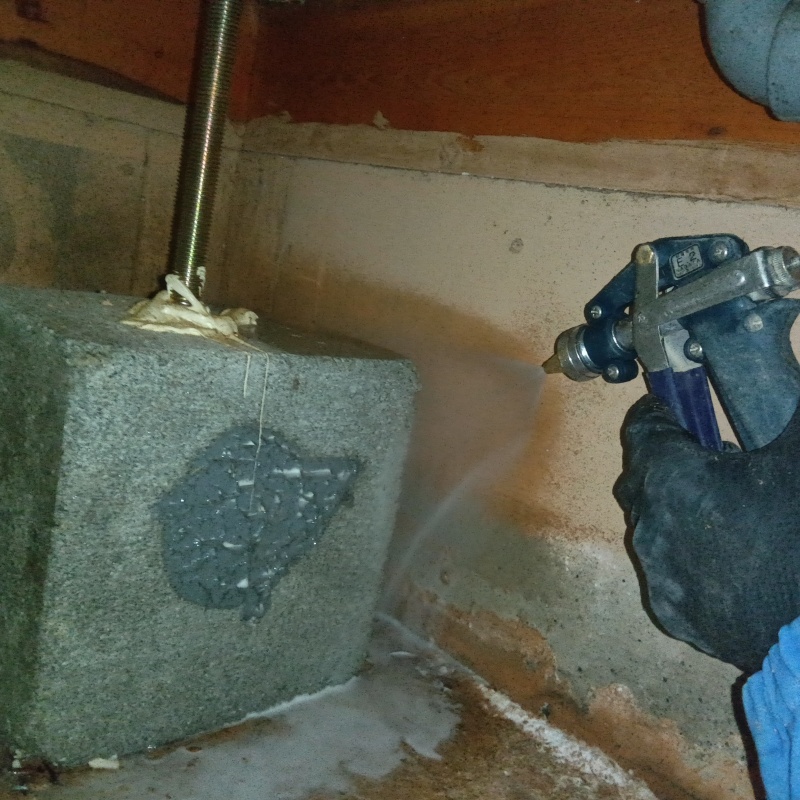 束石まわりにシロアリ駆除剤を吹きつけている様子