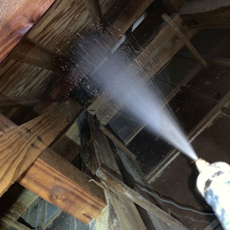 屋根裏の木材にシロアリ駆除剤を散布する様子