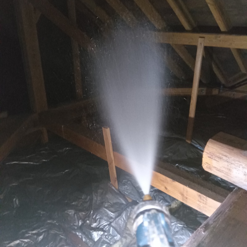 屋根裏の木材にシロアリ駆除剤を吹き付ける様子