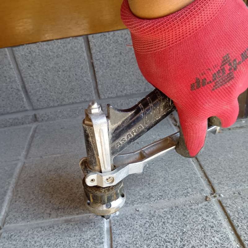 玄関床の目地からシロアリ駆除剤を注入している様子